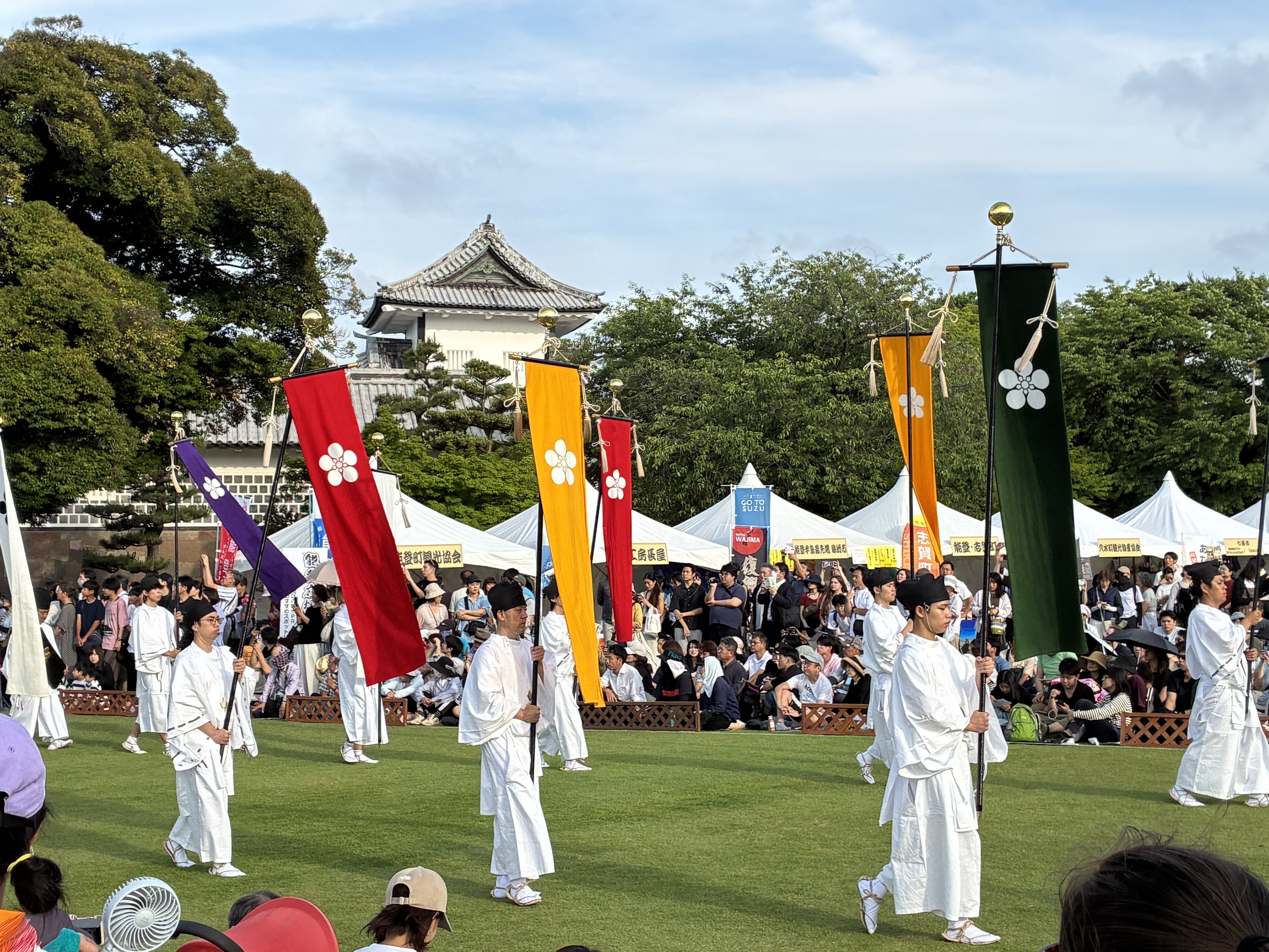金沢城公園・三の丸広場を進む百万石行列。梅鉢紋の旗と城の櫓が映える