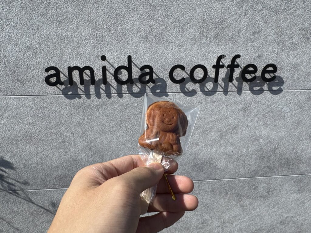 amida coffeeの看板の前で手に持った棒付きの大仏カステラ